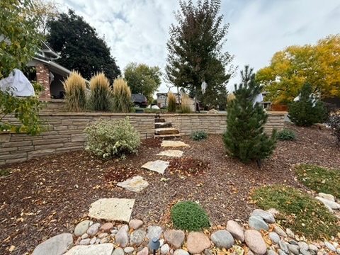 Stone retaining wall with ornamental grasses above a flagstone path and river rock beds