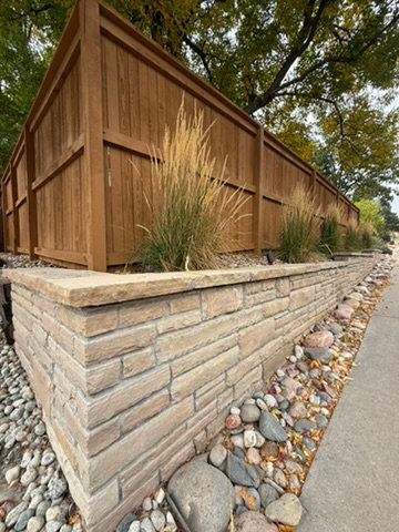Stacked-stone retaining wall with ornamental grasses along a cedar fence