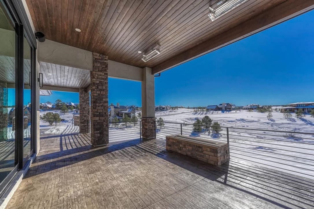 Covered stamped concrete patio with stone columns and cable railing in winter