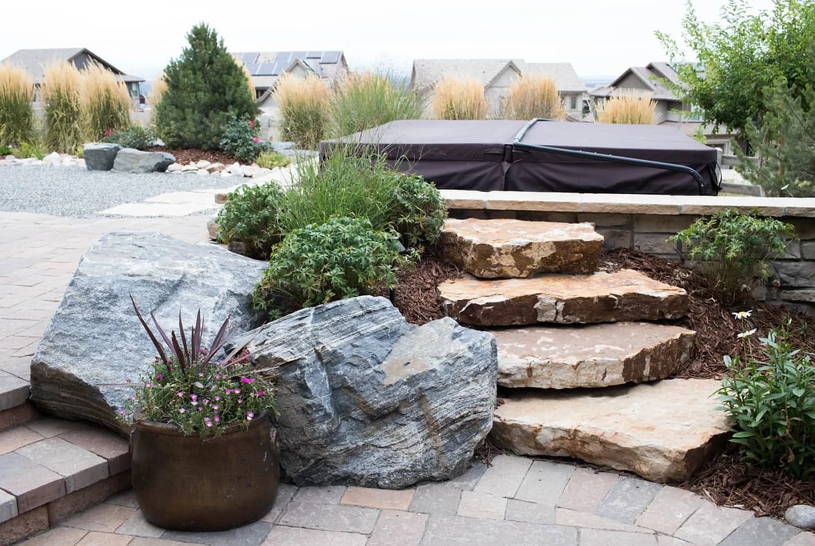 Boulders and sandstone steps beside a paver patio with ornamental grasses and perennials