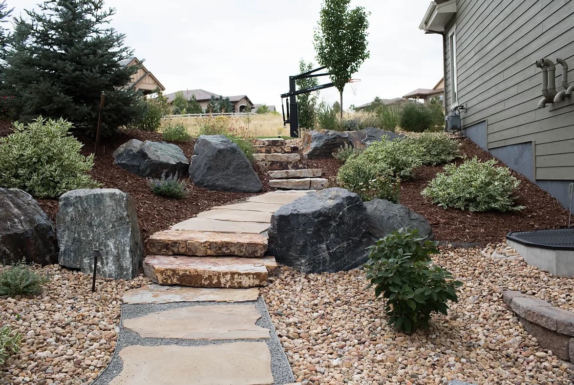 Flagstone path and slab steps through river rock with boulders and shrubs