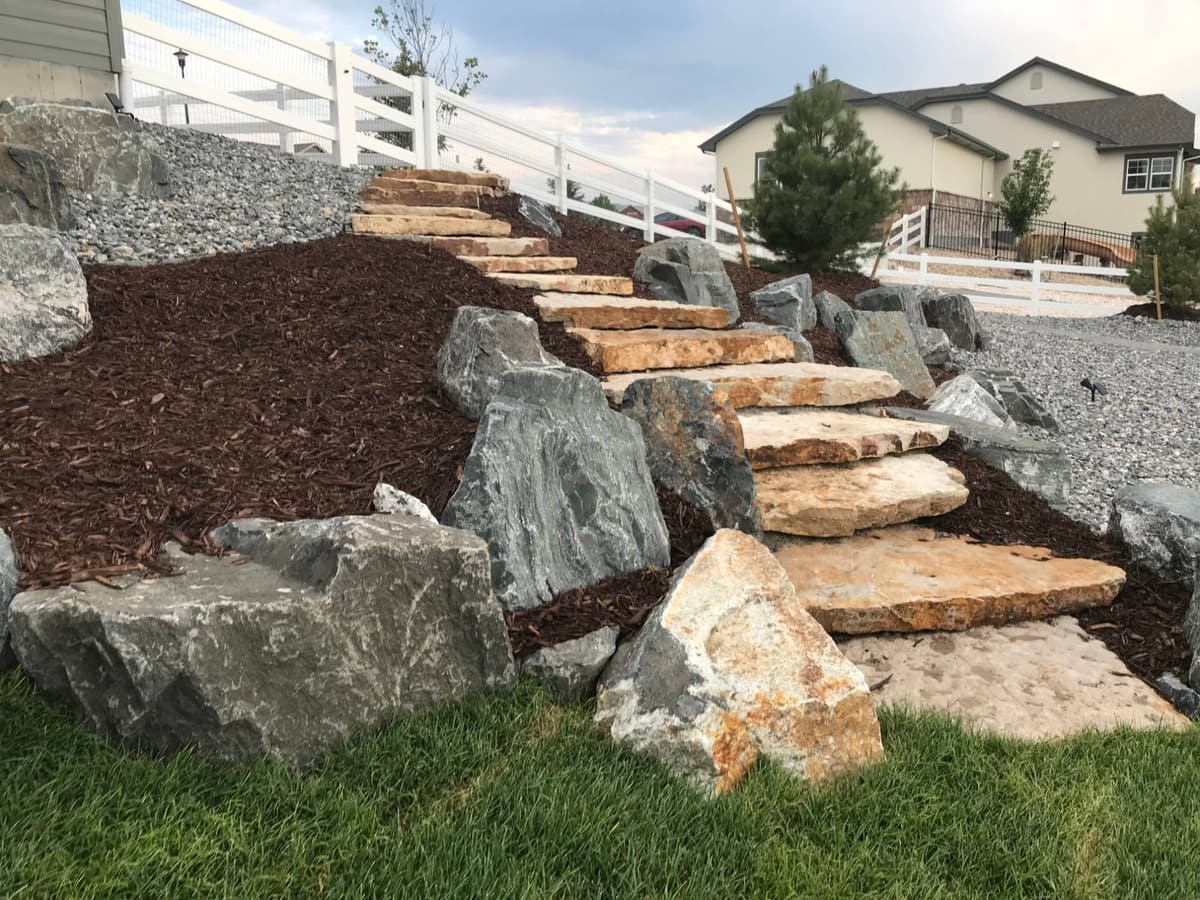 Sandstone slab steps climbing a mulched slope between boulders and rock beds