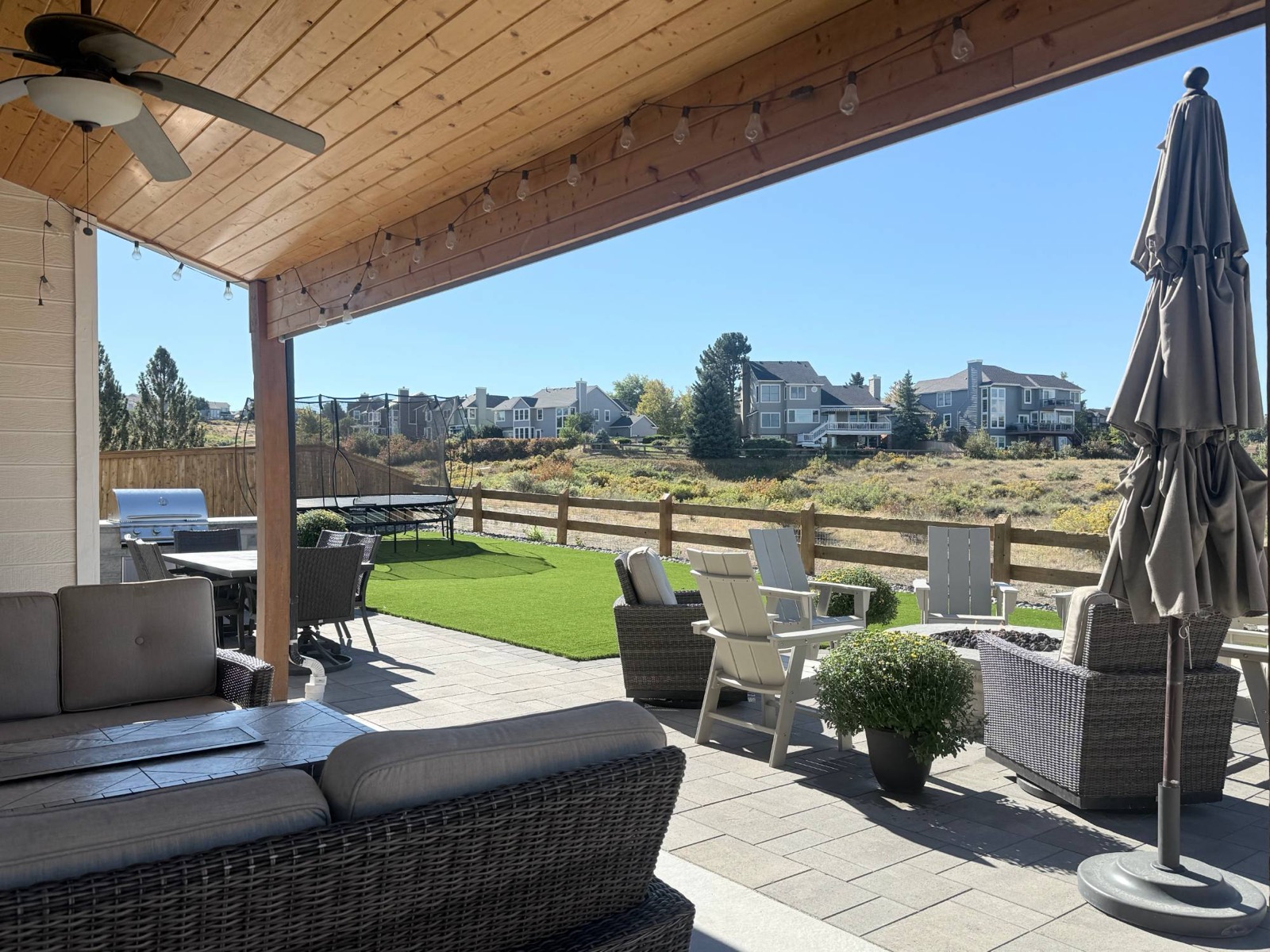 Covered patio with string lights overlooking a paver patio and turf lawn