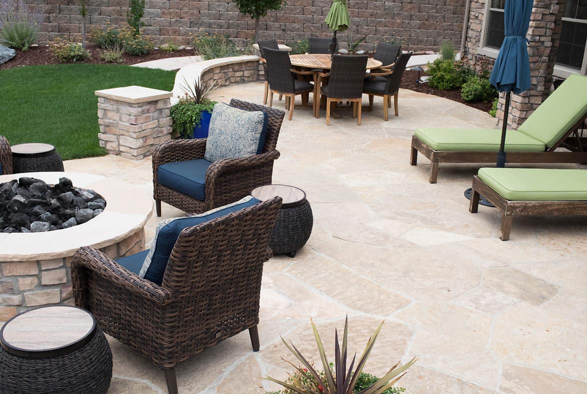 Stone patio with a round fire pit, wicker lounge chairs, dining area and chaise lounges