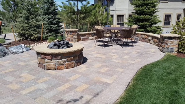 Paver patio with a round stone fire pit, dining area and seat walls