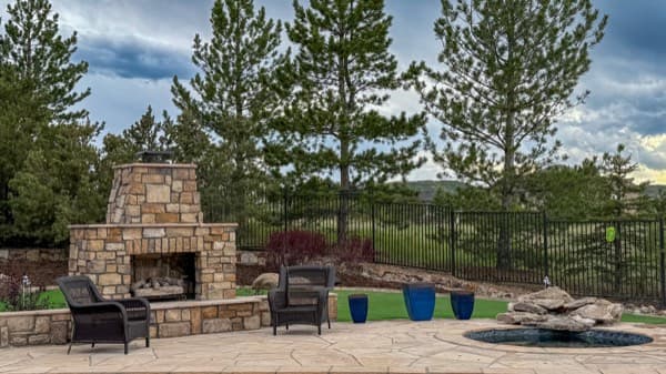 Stacked-stone outdoor fireplace on a stone patio surrounded by pine trees