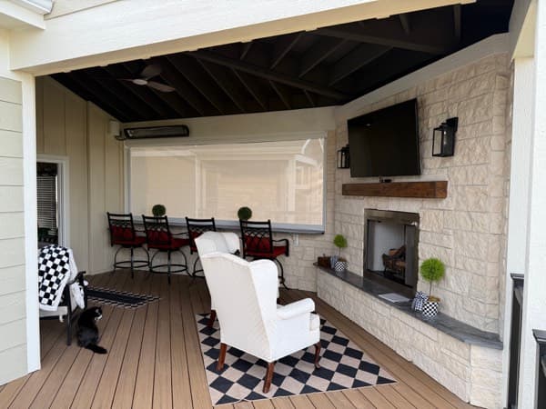 Covered deck with a stone fireplace, TV wall and bar seating