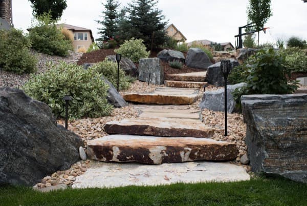 Stone slab steps with path lights winding through boulders and shrubs