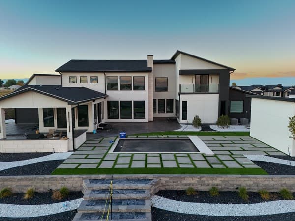 Modern backyard with a geometric paver and turf grid, retaining walls and stone steps at dusk