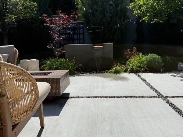 Large-format concrete patio with gravel joints, lounge seating and a wall fountain