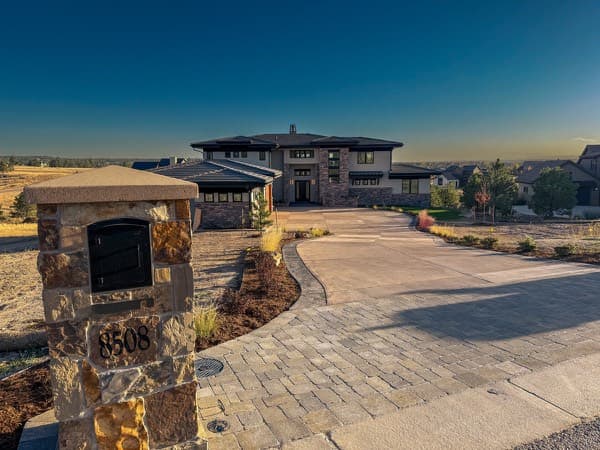 Stone mailbox column and paver driveway leading to a modern home