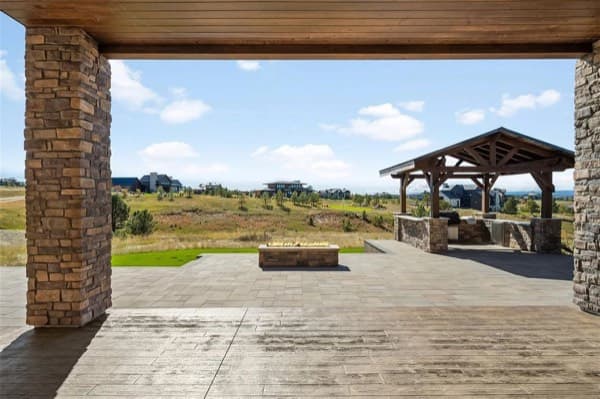 Covered stamped-concrete patio with stone columns overlooking a timber pavilion